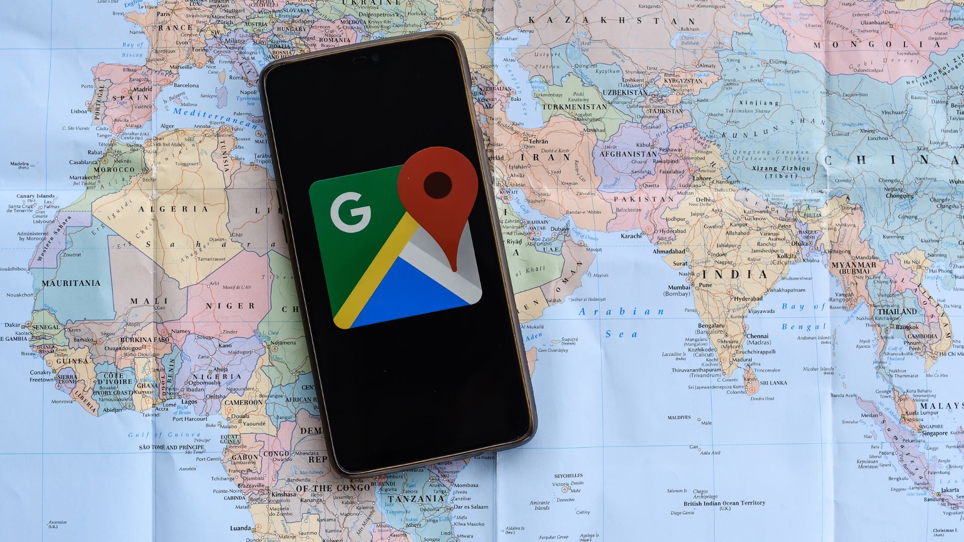 Google Mapsのアイコンが表示されたスマートフォンと世界地図