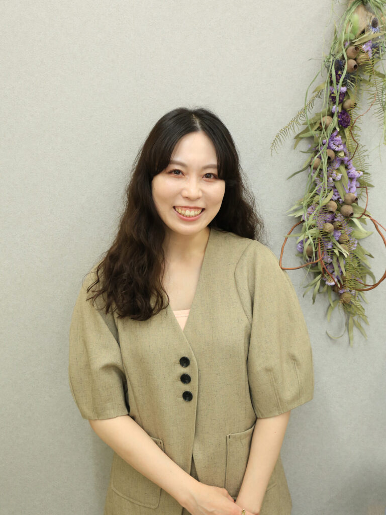アイデザイン ツツ. 代表Luna様のポートレート写真。カーキ色のジャケットを着用し、笑顔で写るプロフェッショナルな一枚